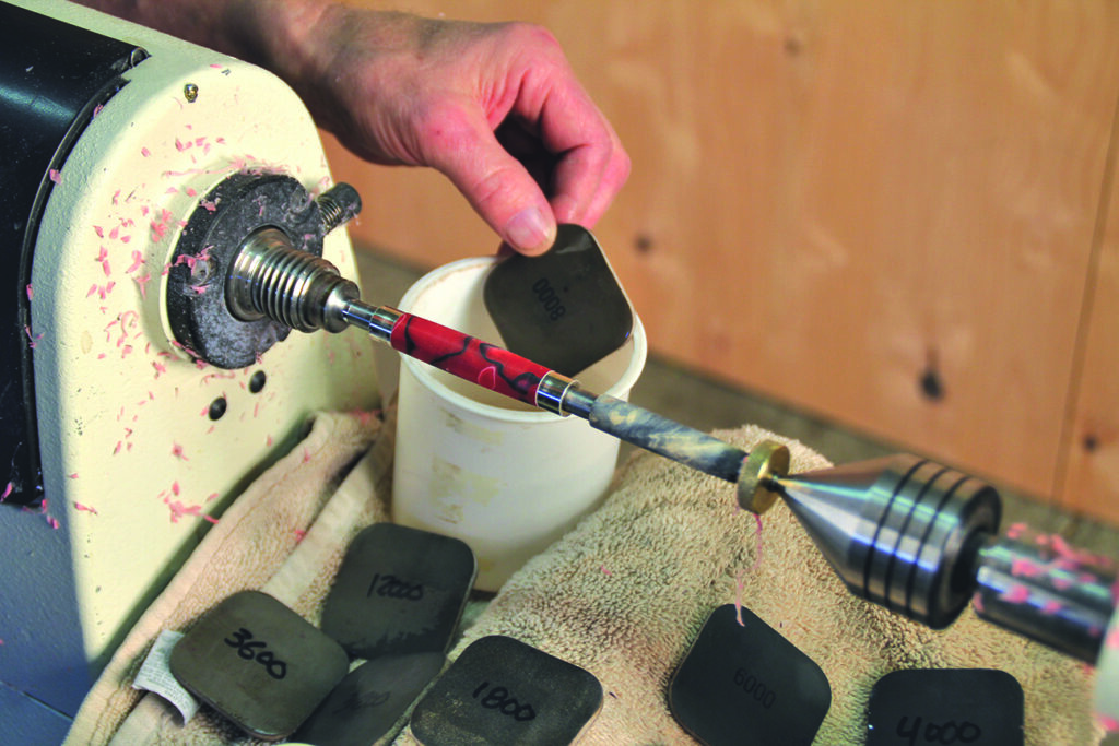 Hand polishing pen with sandpaper on lathe.