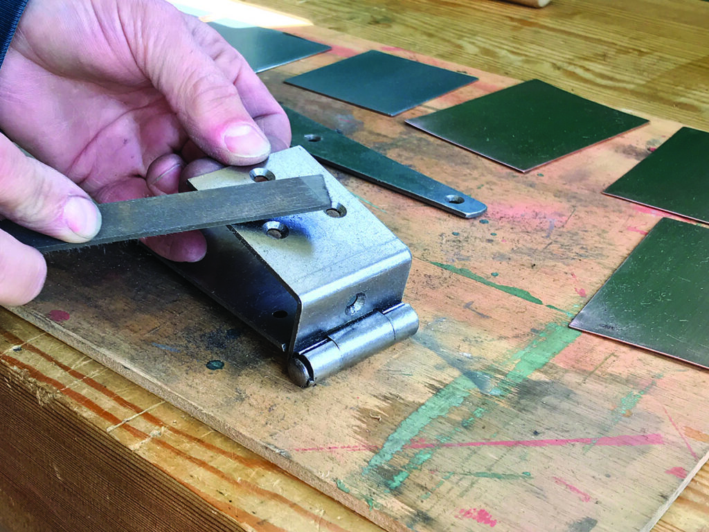 Hand filing metal hinge on wooden table.