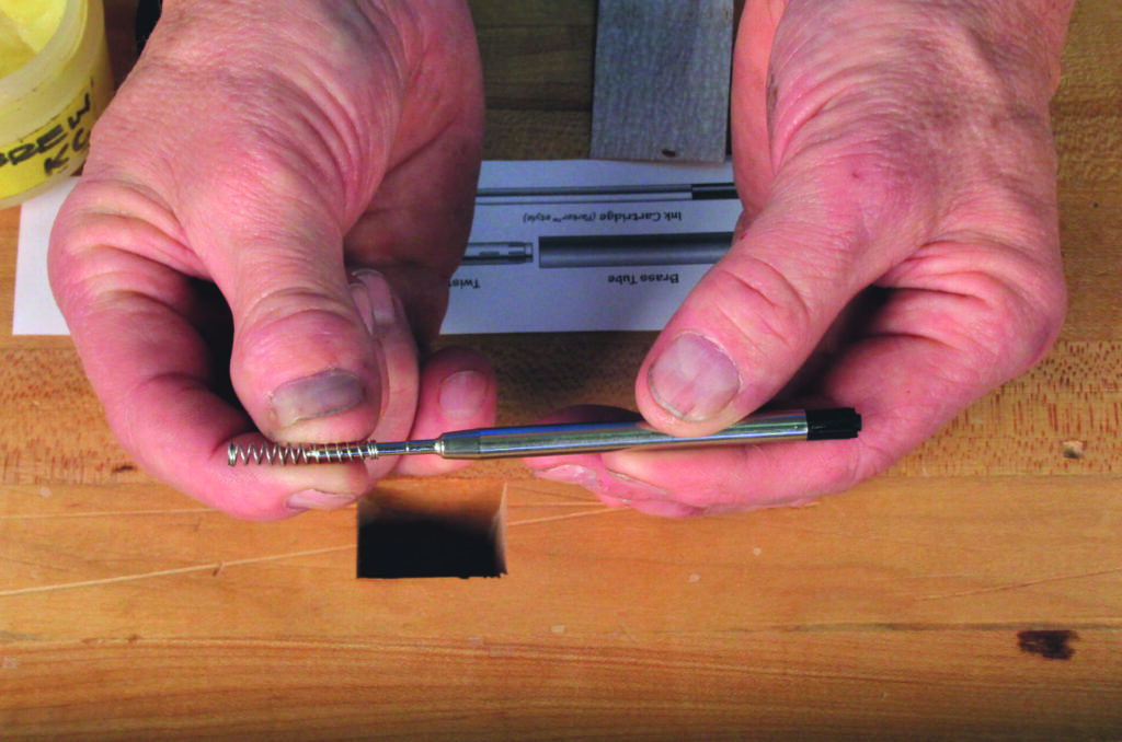 Hands assembling pen parts on wooden surface.