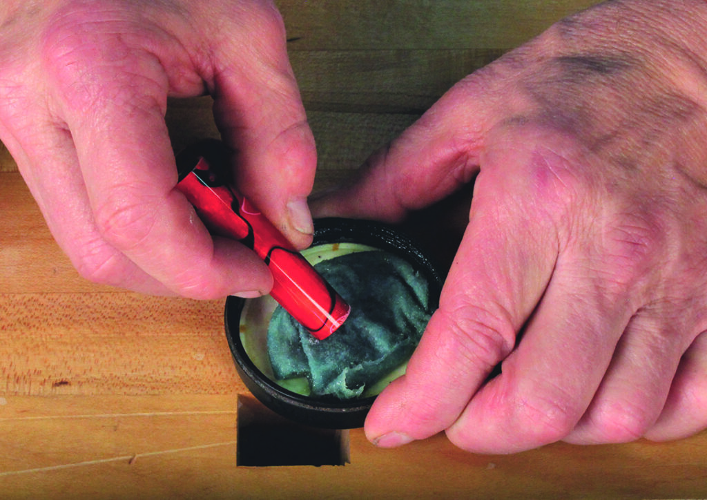 Applying metal polish with red tool on wood