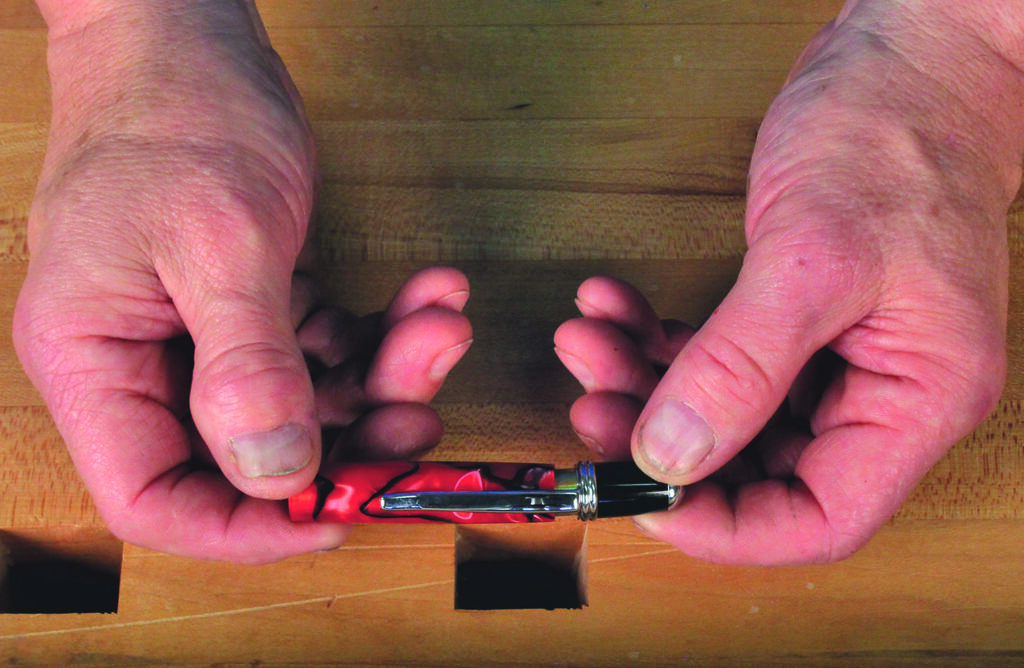Hands holding a red pen on wooden table.