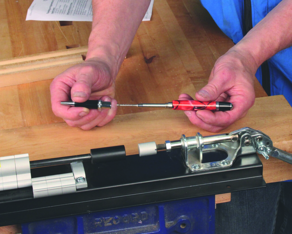 Person assembling a pen using tools on workbench.
