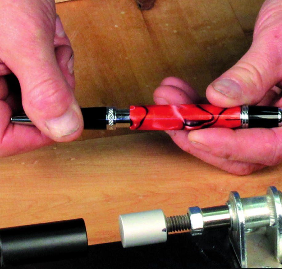 Hand holding a red handcrafted pen on table.
