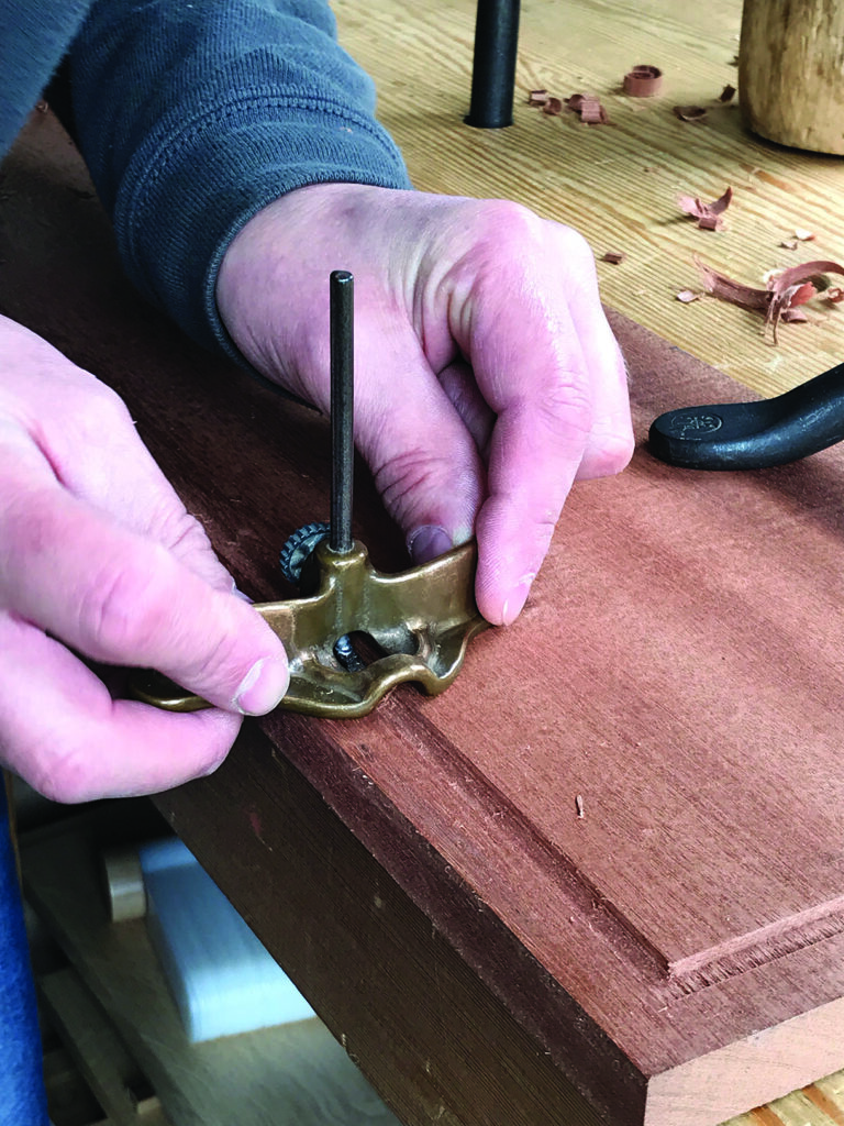 Hand securing woodworking tool on wooden plank.