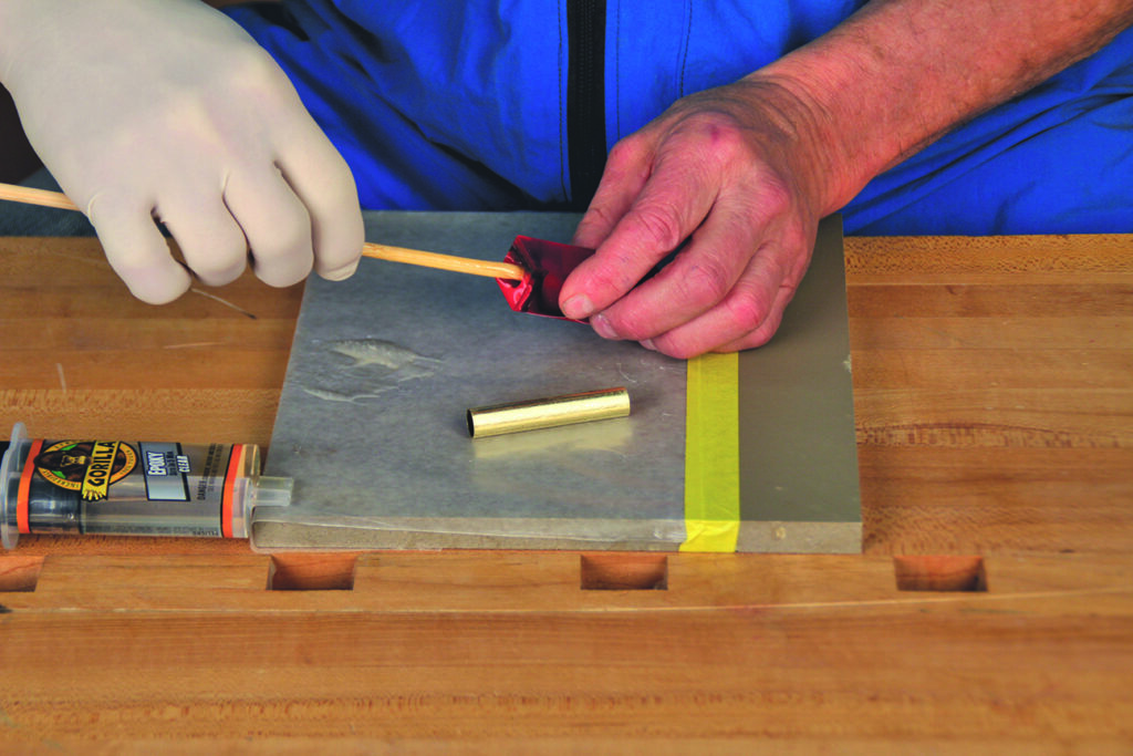 Applying epoxy to metal tube on workbench.