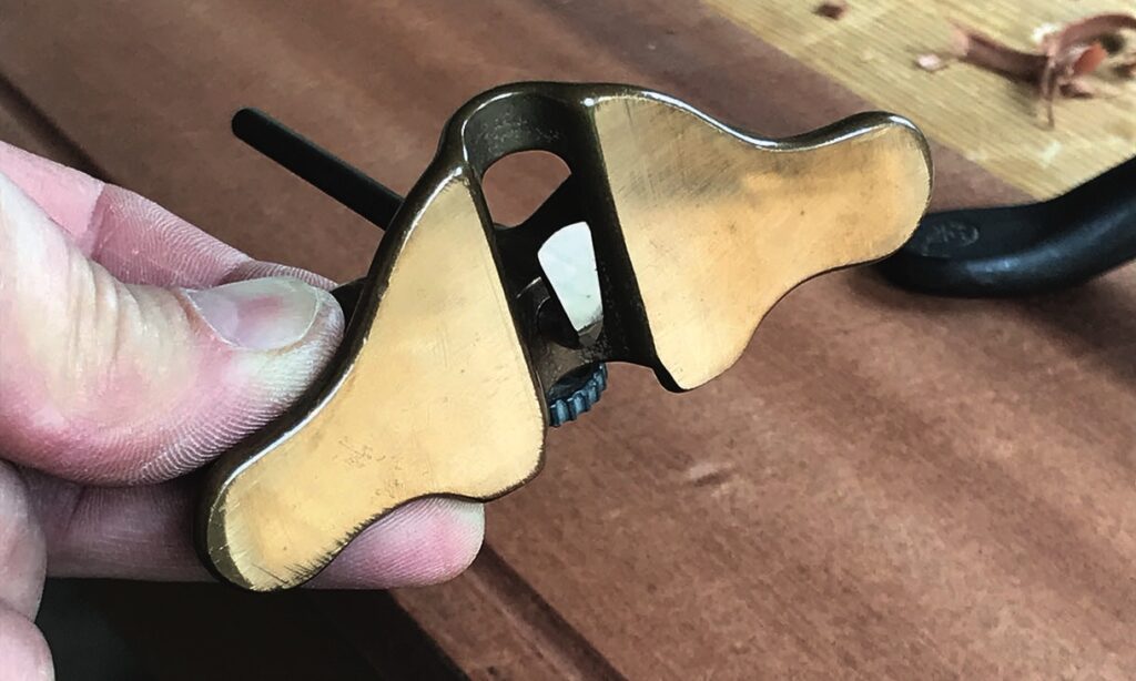 Hand holding brass plane tool on wood surface.