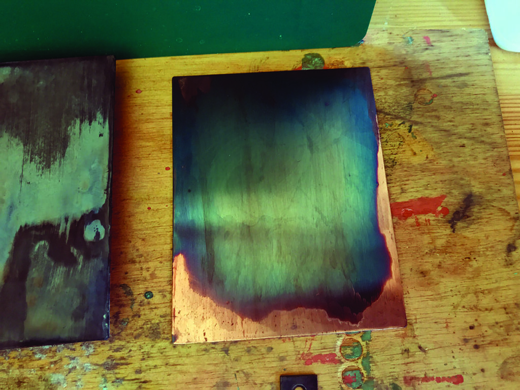 Copper plates on wooden table, artistic patina shown.
