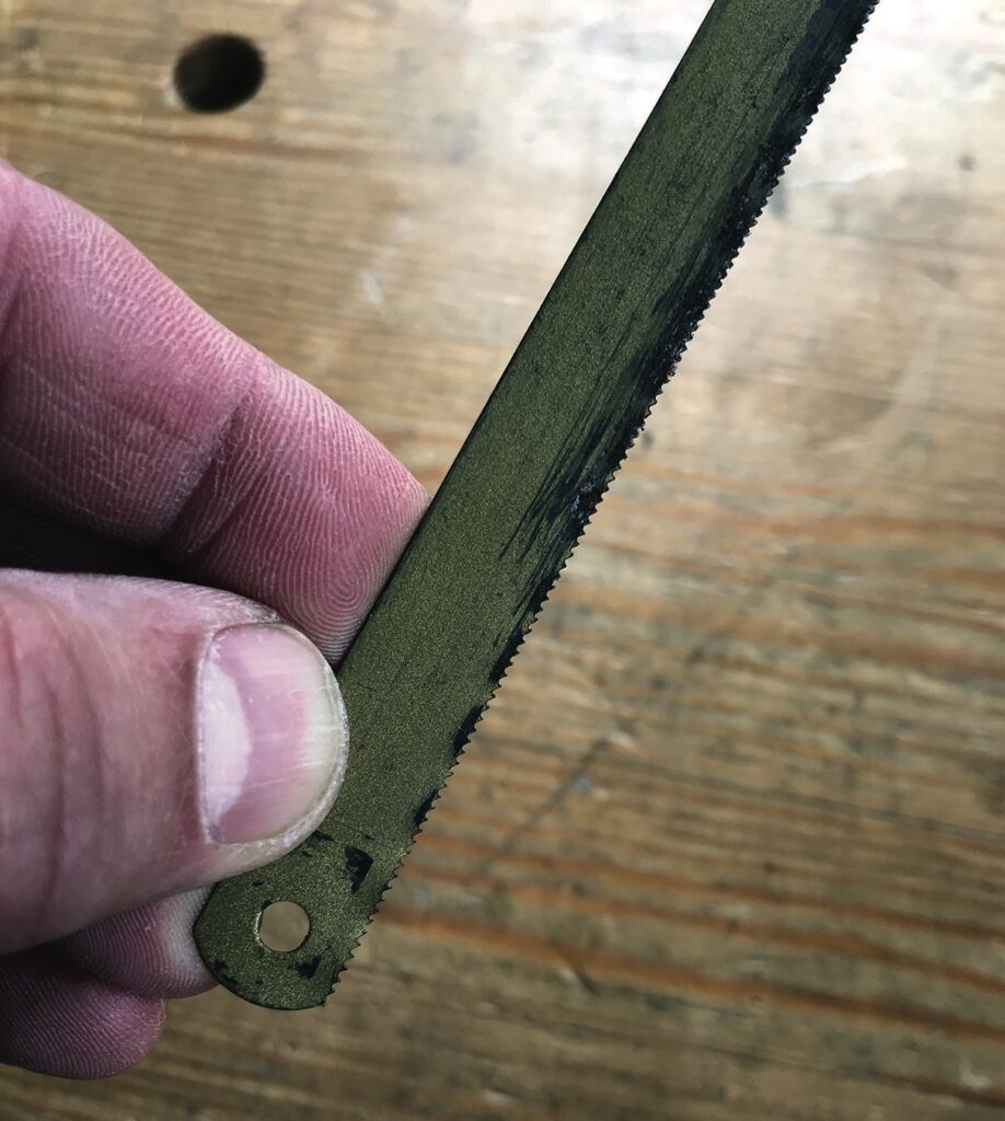 Hand holding a small metal saw blade.