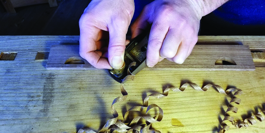 Craftsman planing wood on workbench.