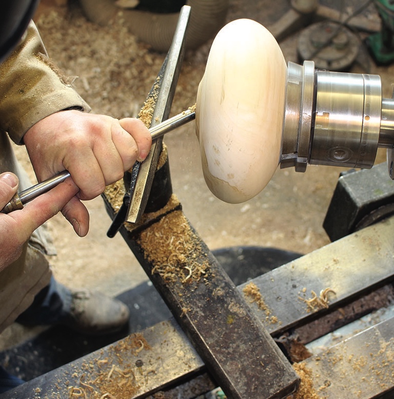Woodturning on lathe with tools and shavings.