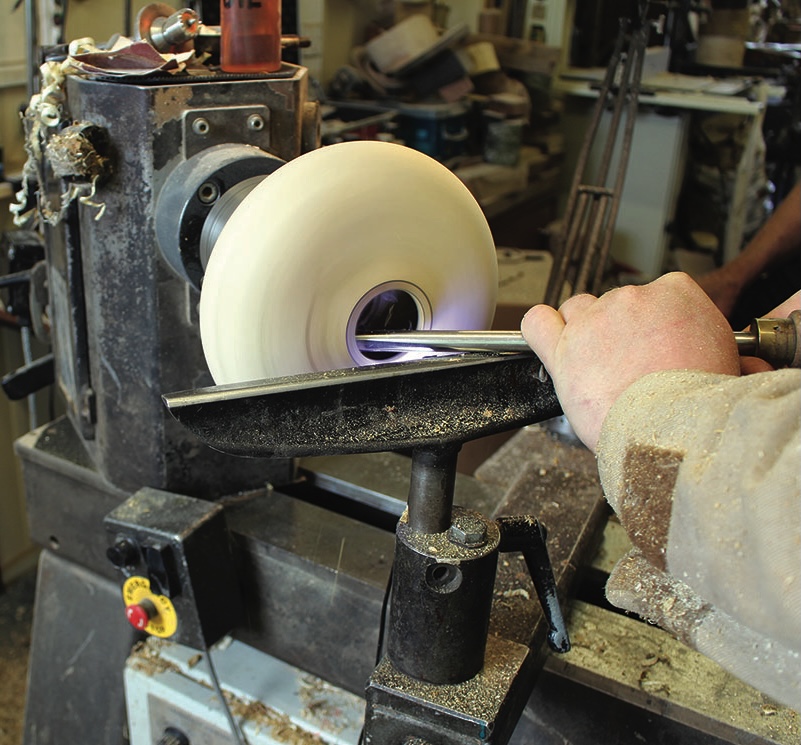 Person carving wood on lathe machine in workshop.