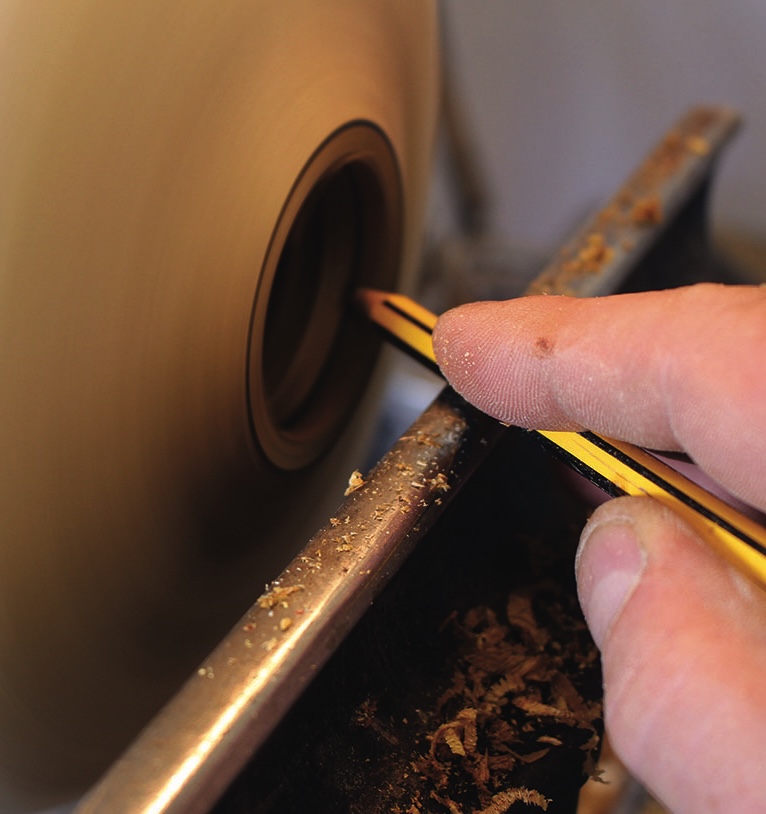 Person creating a pencil with a lathe tool.