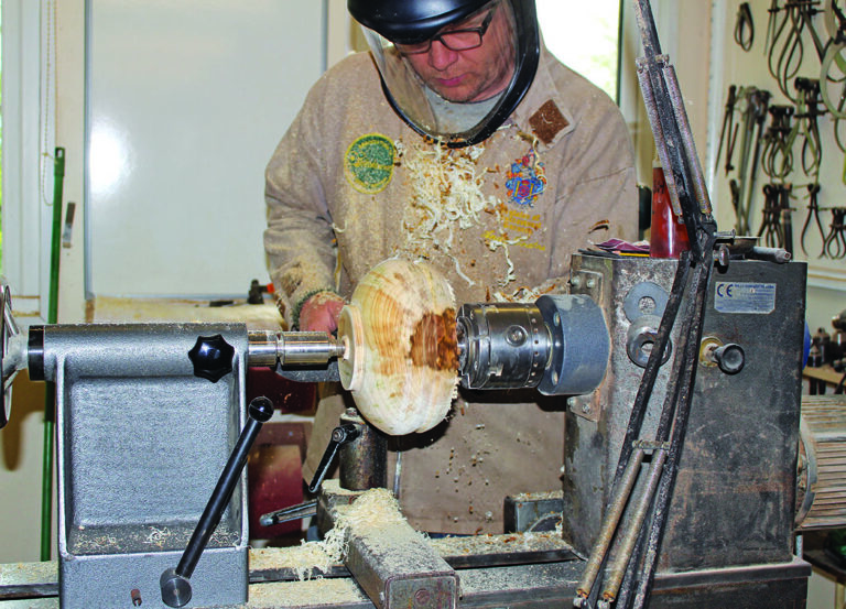 Woodturner shaping a bowl on a lathe.