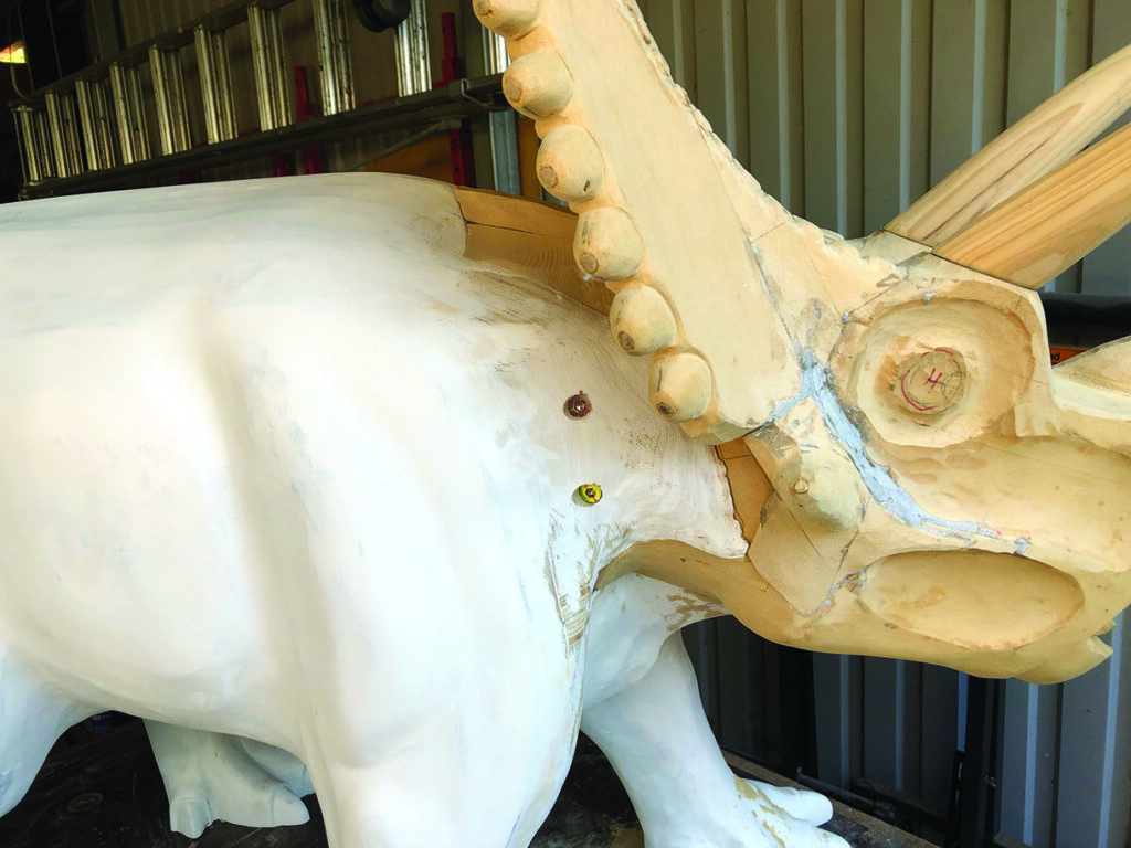 Wooden dinosaur sculpture under construction in workshop.