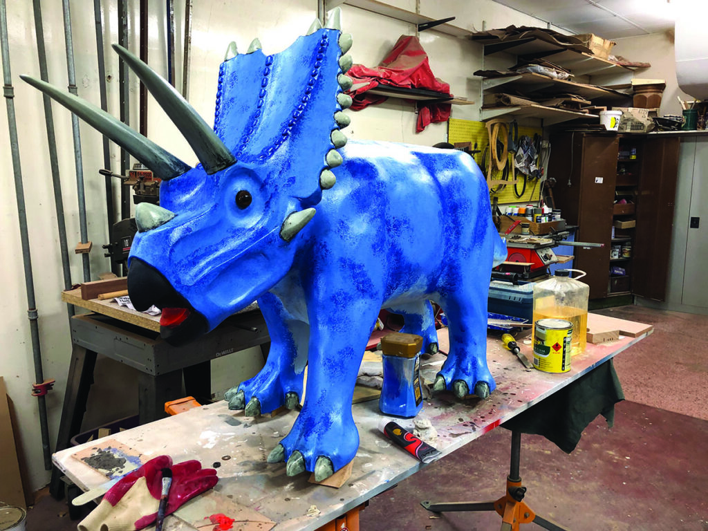 Blue triceratops sculpture in workshop setting.