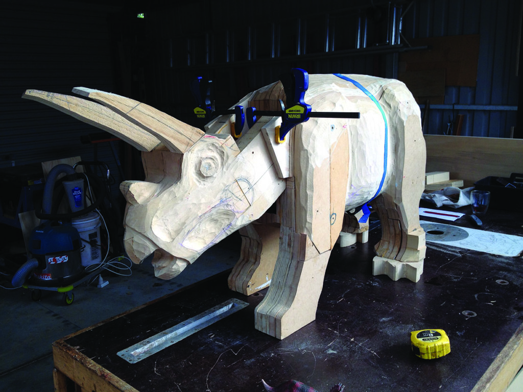 Wooden triceratops sculpture being crafted in workshop.