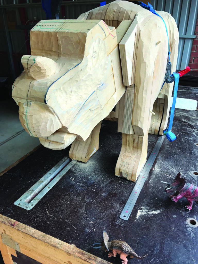 Wooden dinosaur sculpture on workbench with toy dinosaurs.