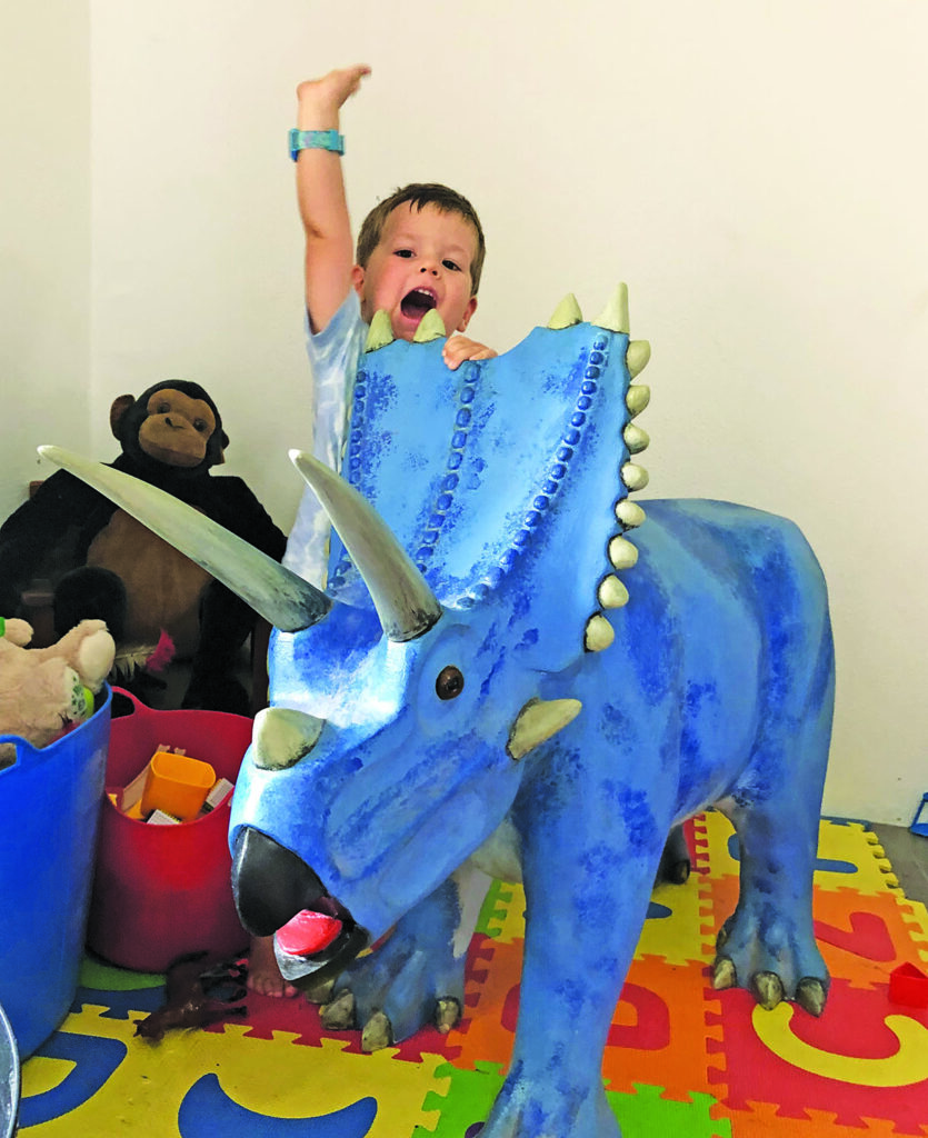 Child playing on blue dinosaur toy in playroom.