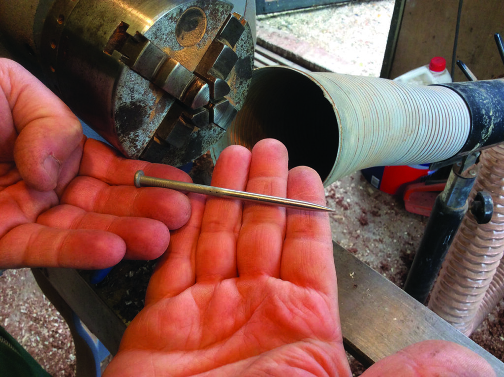 Hand holding metal nail near lathe machine.