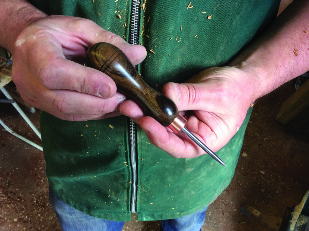 Person holding a wooden-handled awl tool.