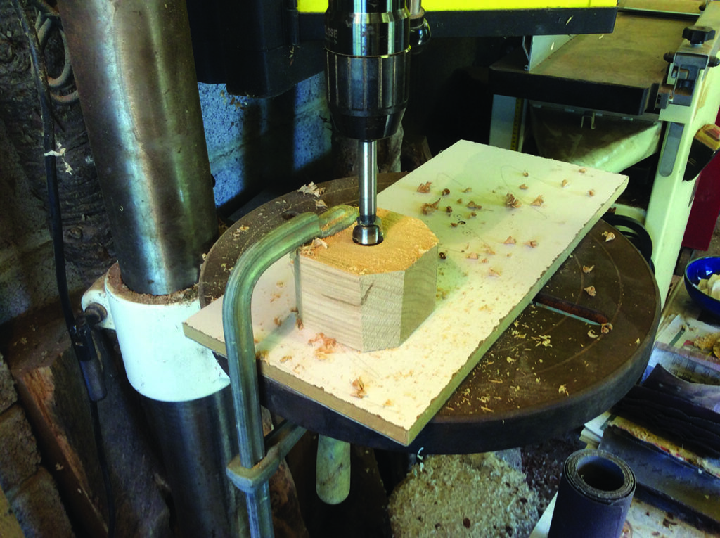 Drill press working on wooden block in workshop.