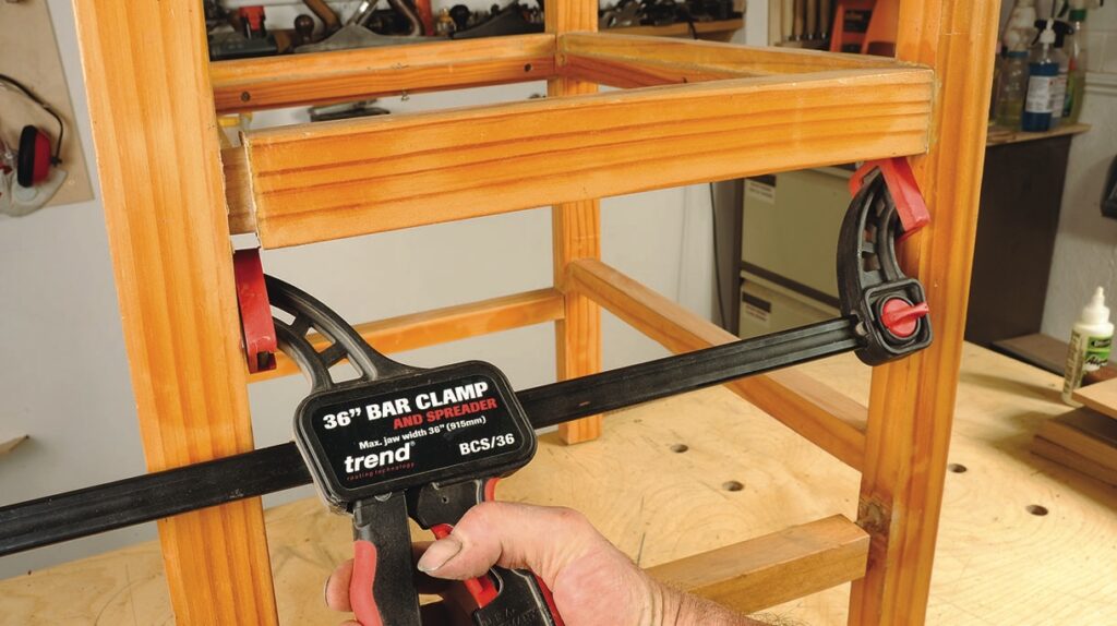 Bar clamp securing wooden structure in workshop.