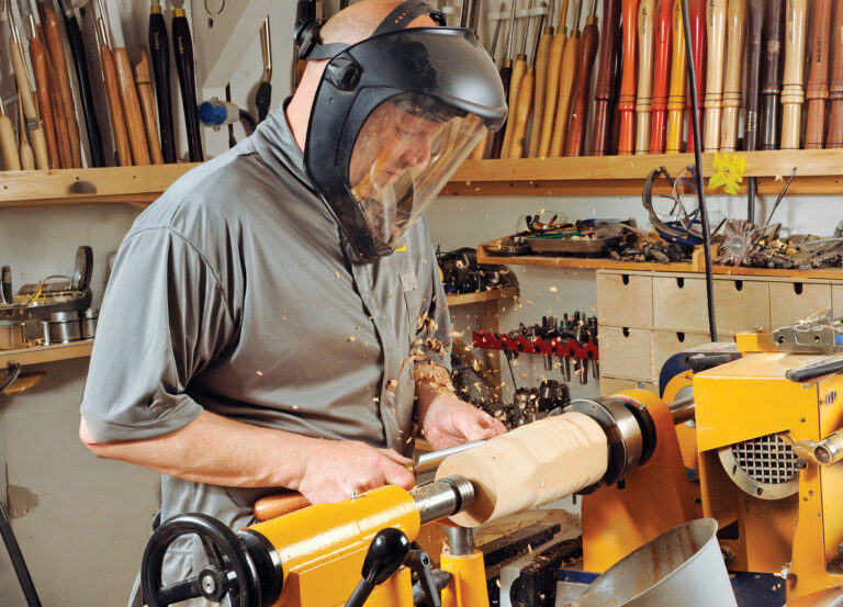 Man woodworking with lathe in workshop.