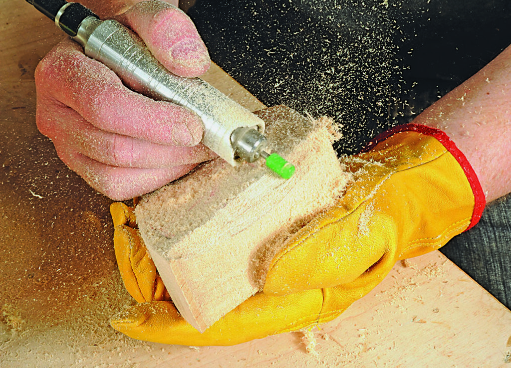 Carving wood with power tool, wearing safety gloves.