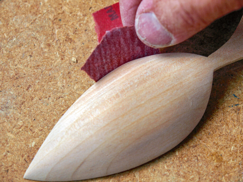 Sanding wooden spoon with red sandpaper sheet.