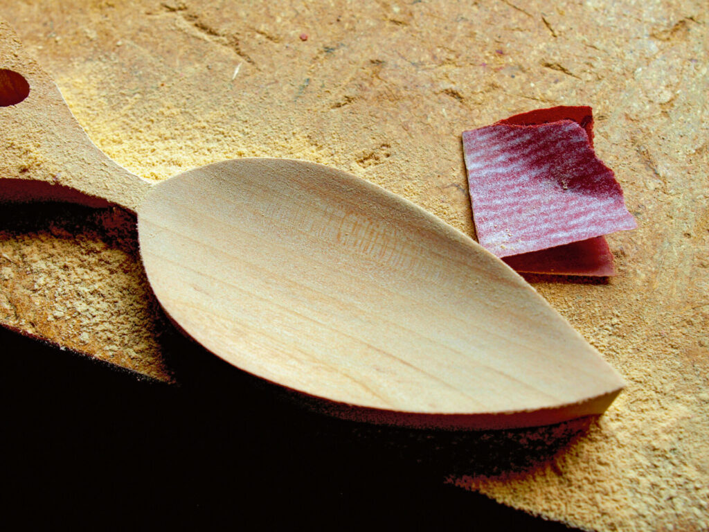 Wooden spoon being sanded with sandpaper.