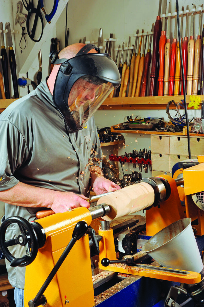 Woodturner shaping wood on a lathe, wearing safety gear.