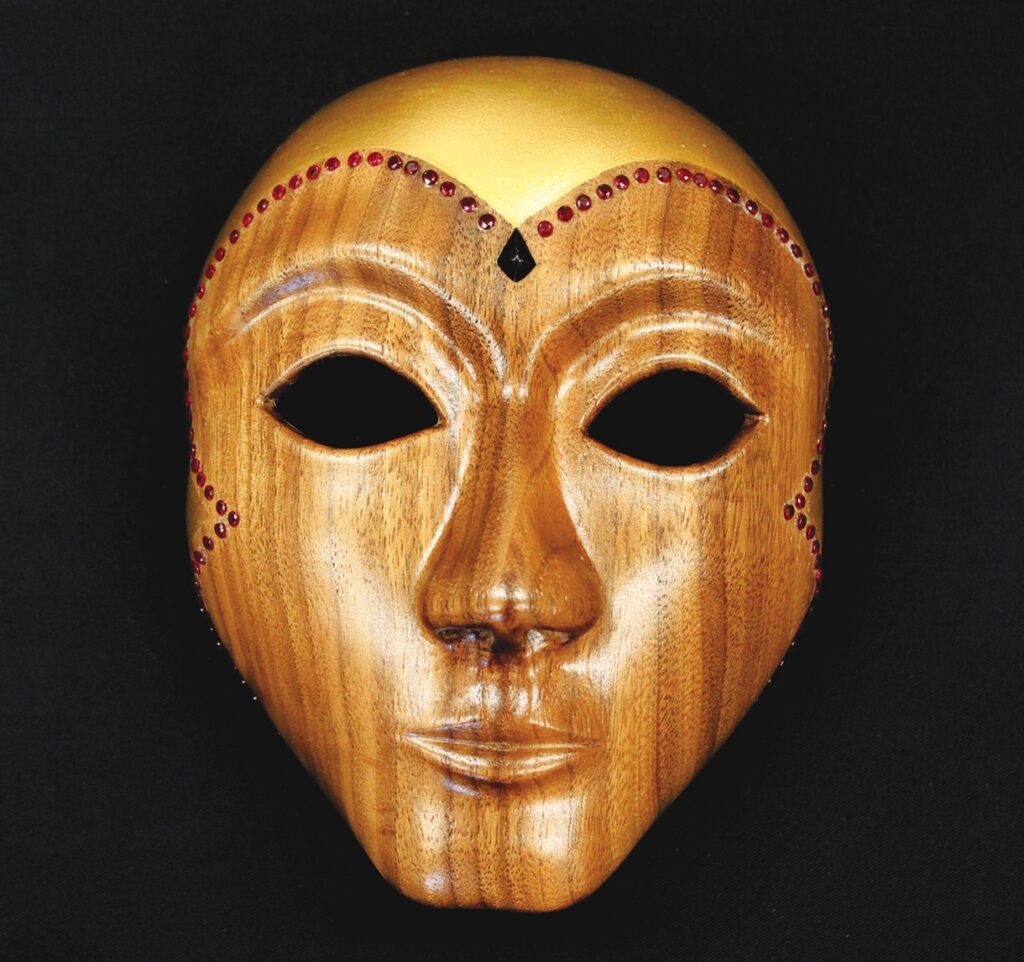 Wooden mask with jeweled decorations on black background.