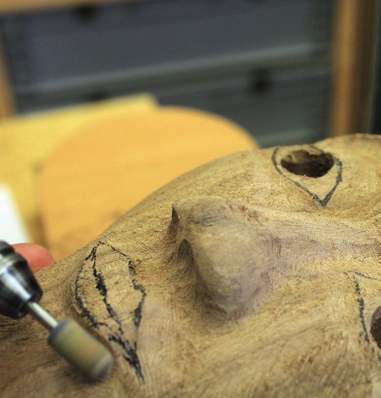 Carving details on wooden mask with tool.