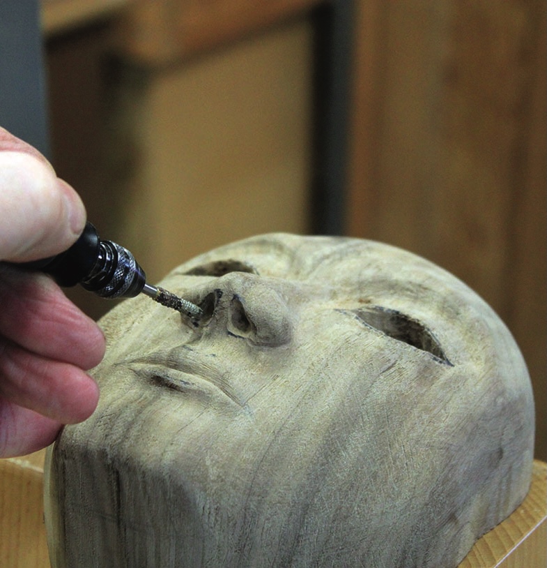 Hand carving details on wooden face sculpture.