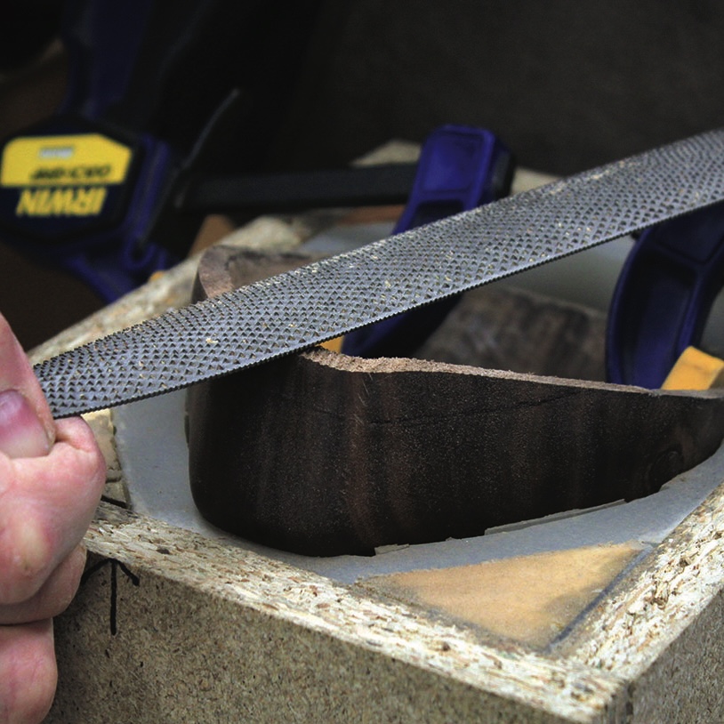 Hand filing wood with carpenter's rasp tool.