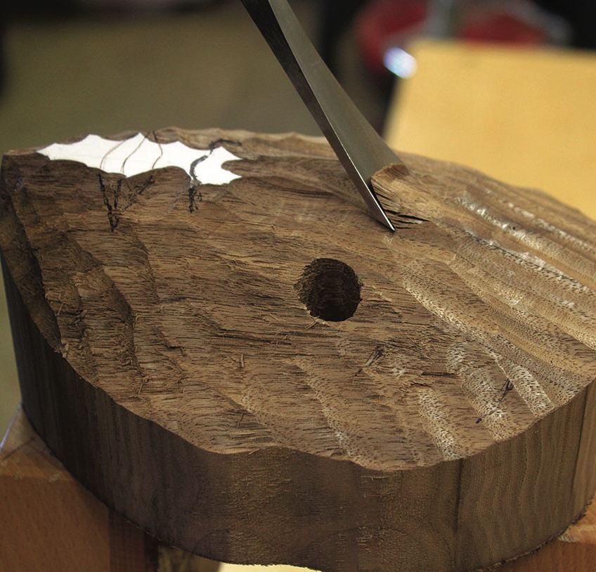 Chisel carving into textured wooden block.