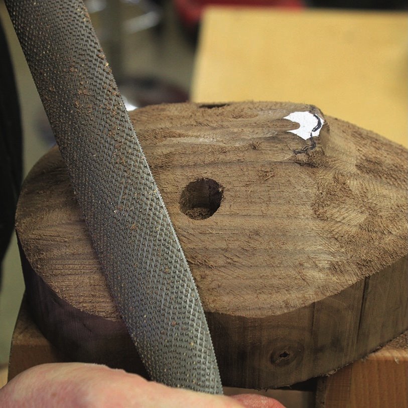 Hand filing wood block with metal file tool.