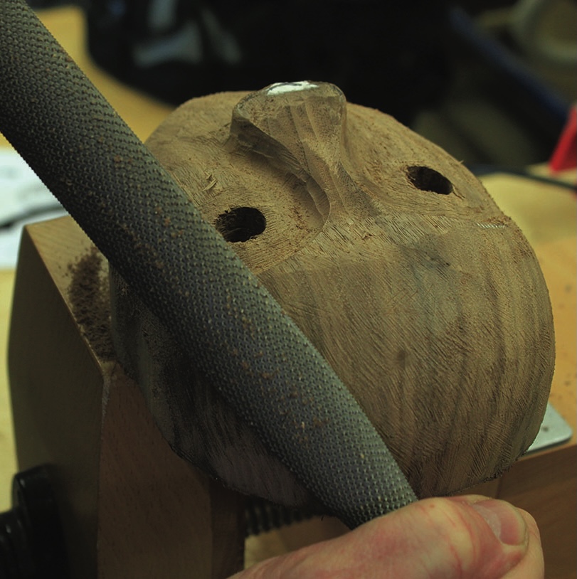 Hand carving wood with a rasp tool.