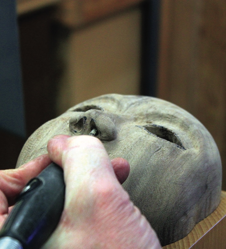 Hand carving details into a wooden mask statue.