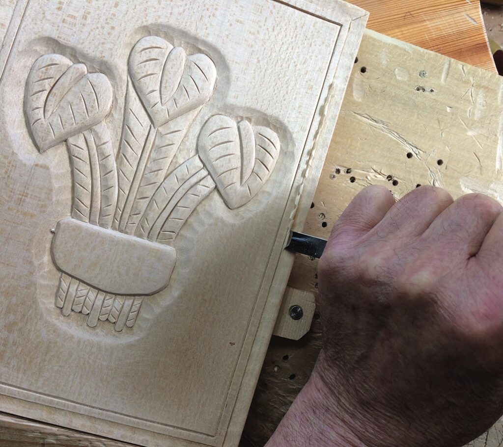 Hand carving floral design into wood panel.