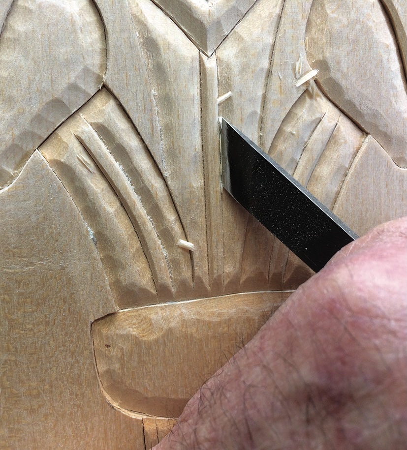 Hand carving intricate wood patterns with chisel.