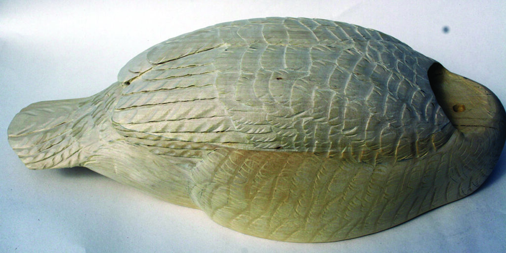 Wooden duck decoy with intricately carved feathers.
