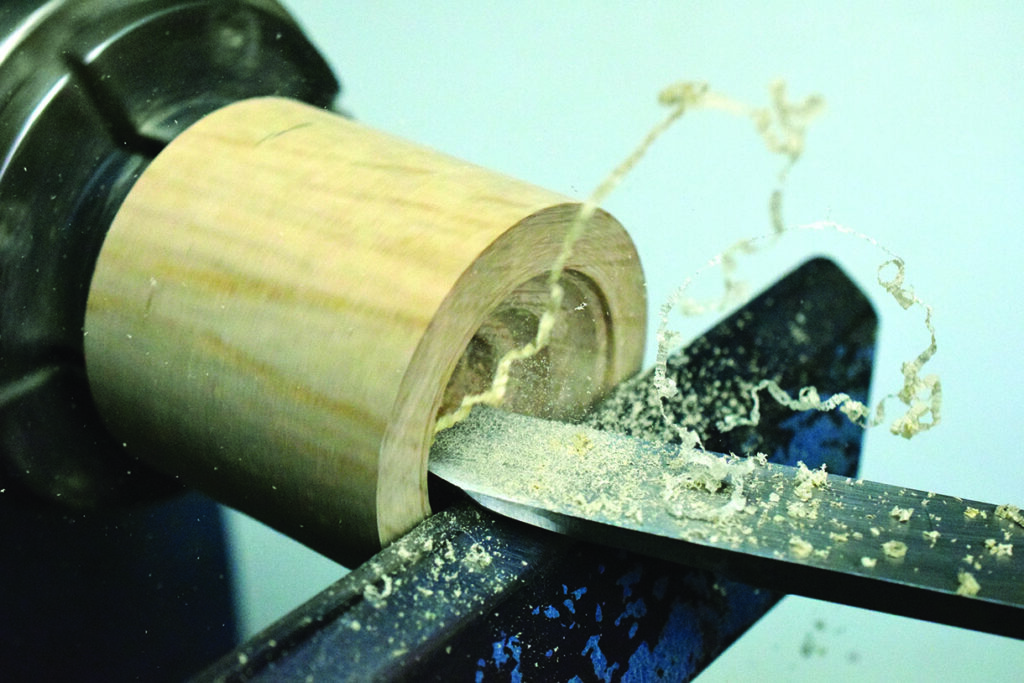 Lathe shaping wooden tube with tool.