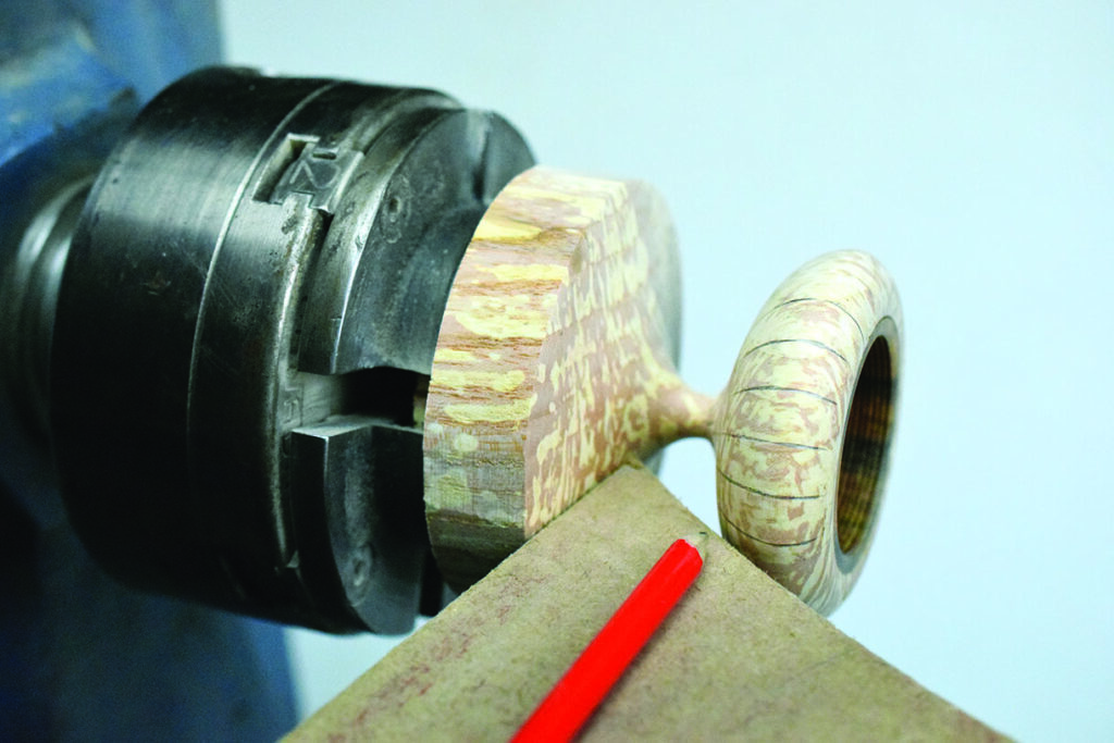 Woodturning lathe with wooden object and red pencil.