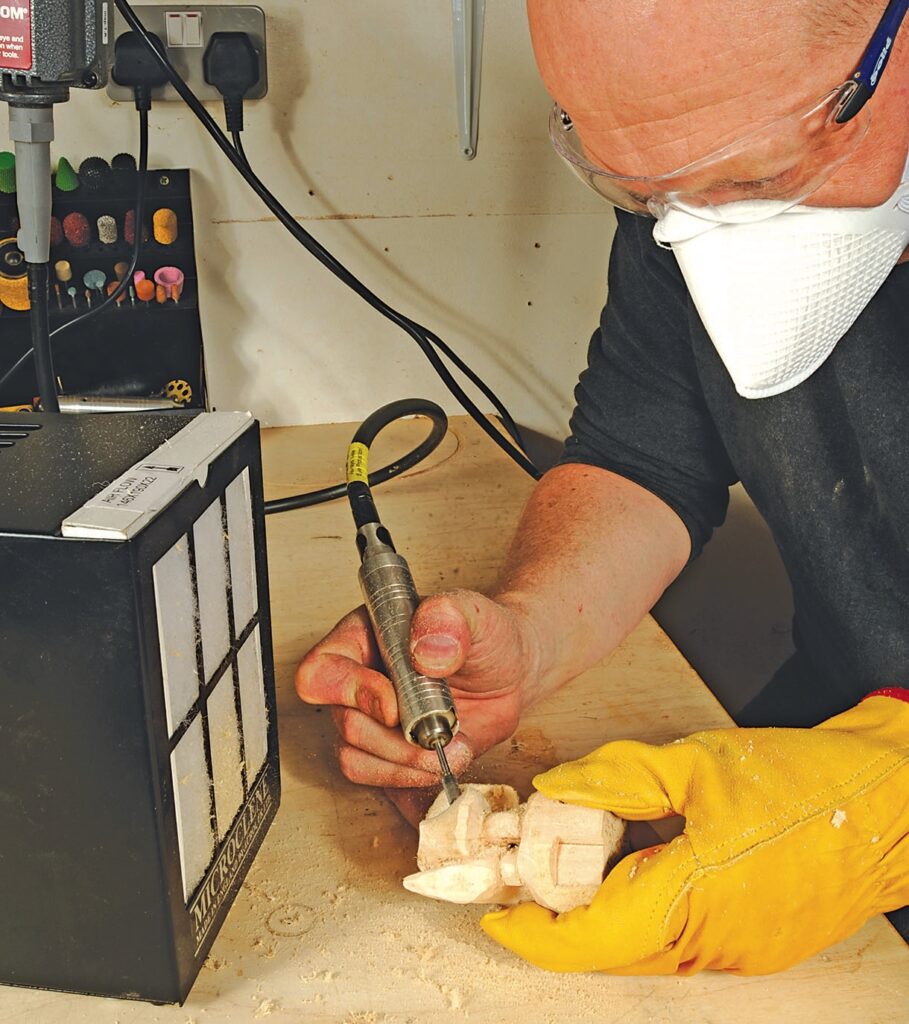 Person carving wood with rotary tool in workshop.