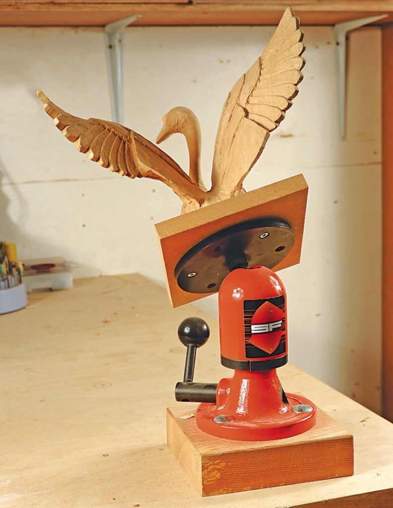 Wooden swan carving on a red tabletop vise.
