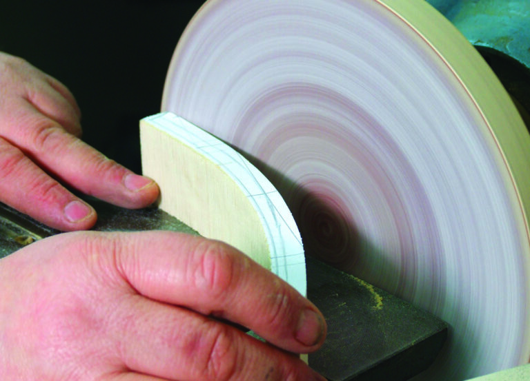 Hands sanding wood block on disc sander.