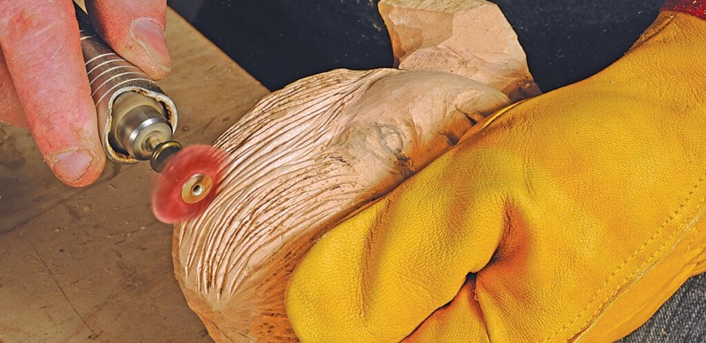 Carving wood with rotary tool, hand wears glove.