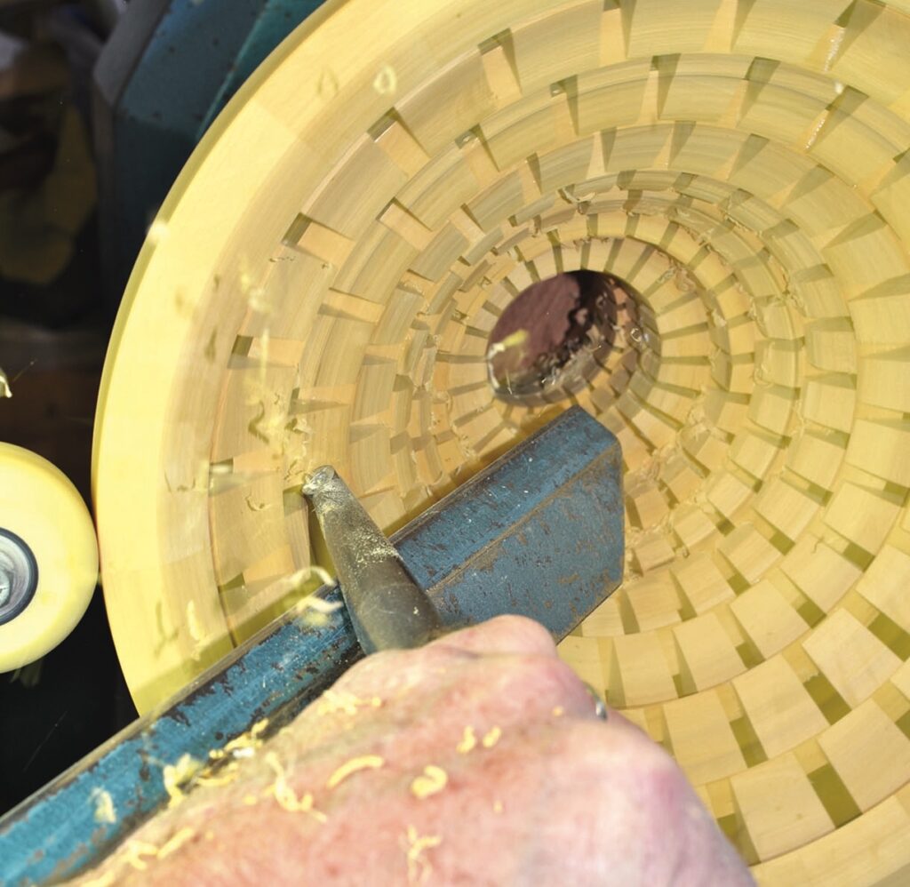 Woodturning with lathe tool on segmented bowl.