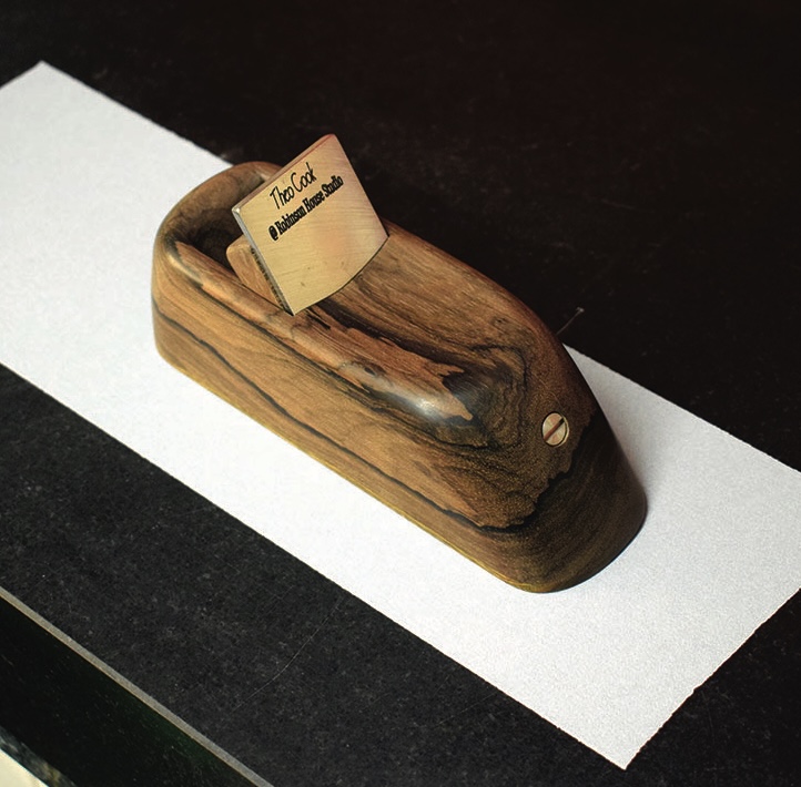 Wooden hand plane on dark surface with white paper.